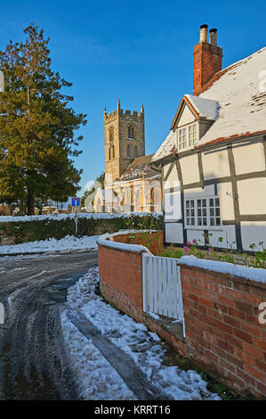 St Peter's church, Welford on Avon, and half timbered black and white cottage on a winter morning, with blue sky following a light snowfall. Stock Photo