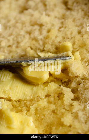 Close up of knife spreading butter on warm fresh bread slice. Stock Photo