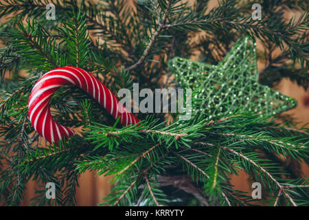 Red candy cane on a natural Christmas tree with green glittering star on the background Stock Photo