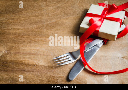 Present and Cutlery Decorated with Red Ribbon on Wooden Background. Stock Photo