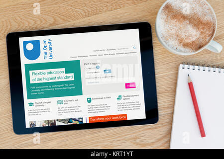 The Open University website on an iPad tablet device which rests on a wooden table beside a notepad and pencil and a cup of coffee (Editorial only) Stock Photo