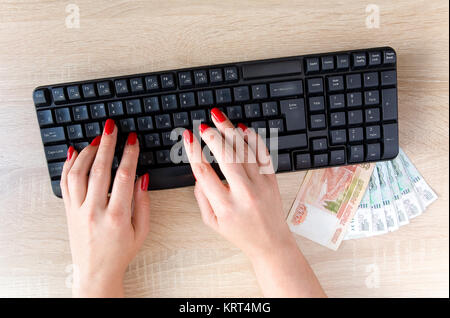Female hands with red nails on a computer keyboard. Against the background of the texture of the tree. Stock Photo