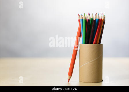 Pencils in a container on a wooden table. Accessories for drawing in a paper mug on a wooden drawing table. White background Stock Photo