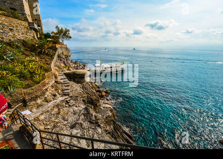 Rocky coastline and trail at the shore of Monterosso Al Mare in Cinque Terre Italy with a cruise or tour boat in the colorful sea Stock Photo
