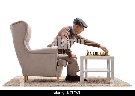 Senior seated in an armchair playing a game of chess with himself isolated on white background Stock Photo