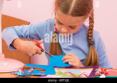 The child cuts off a piece of the blue colored cardboard Stock Photo