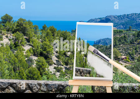 Bemalte Leinwand steht auf einer Staffelei. Auf der Leinwand eine Urlaubslandschaft mit Meer im Hintergrund. Stock Photo