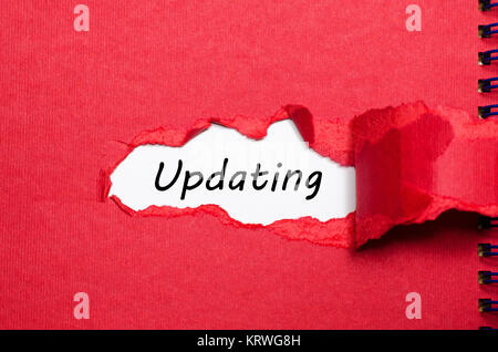 The word updating appearing behind torn paper Stock Photo