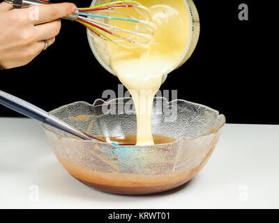 Female person pouring Gogl-Mogl, into a glass bowl with chocolate, with hand whisker from plastic bowl, isolated on black Stock Photo