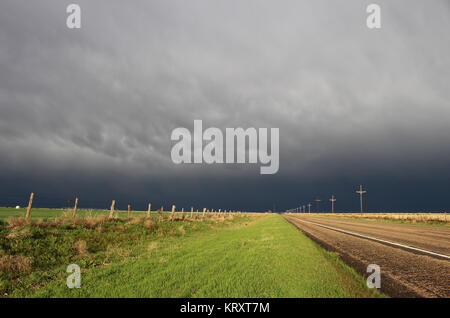 The sun shines brightly along a lonely highway while a dark and stormy sky looms on the horizon. Stock Photo