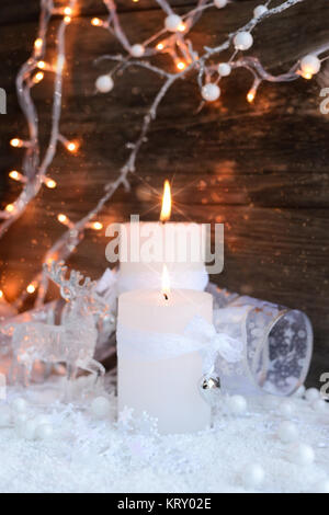 Two burning candles with a deer with christmas decorative balls on snow and Christmas lights. Christmas decorations on wooden background. Stock Photo
