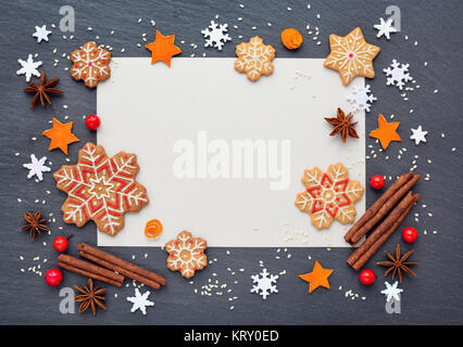 Christmas background with gingerbread cookies, snowflakes, spices and blank sheet of paper for your congratulations on dark table, top view Stock Photo