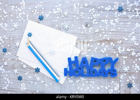 Greeting "Happy Holidays", pencils, envelopes and snowflakes on a light wooden background. Top view. Stock Photo