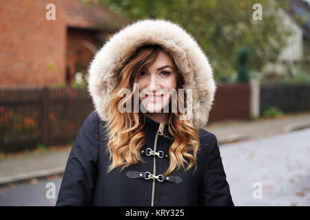 smiling young woman wearing winter coat with fake fur hood Stock Photo