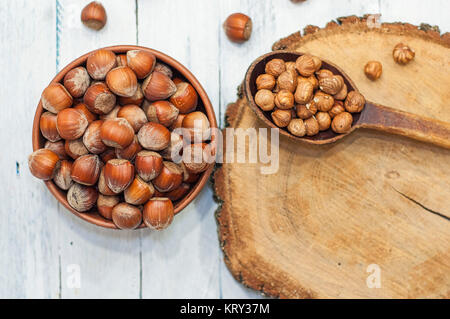 Hazelnuts in a bowl near a spoon peeled walnut on a wooden surface Stock Photo