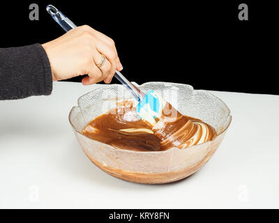 Female person blending chocolate gently with Gogl-Mogl, in a glass bowl on white table towards black Stock Photo