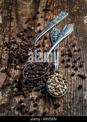 Spices fragrant scented dry peppers peas black and white, cloves dried for cooking poured in three spoons lie on a wooden background Stock Photo