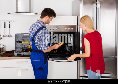 Male Worker Repairing Oven Appliance Using Multimeter Stock Photo