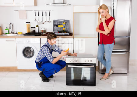 Male Worker Repairing Oven Using Multimeter In Kitchen Stock Photo