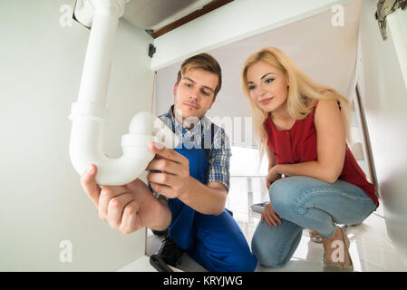 Plumber Showing Damage In Sink Pipe To Woman Stock Photo