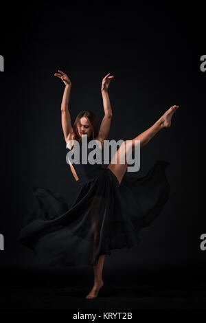 Young beautiful dancer in beige dress dancing on black background Stock Photo