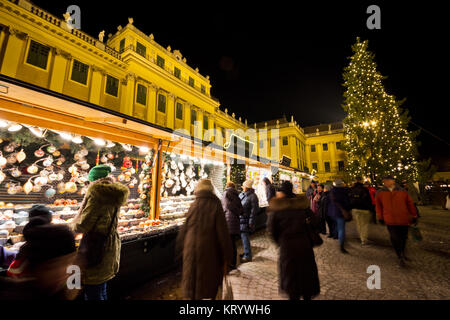 Traditional christmas market with illuminated Schönbrunn palace and fairy lights decorated Christmas tree at dusk, tourists and people in festive mood Stock Photo