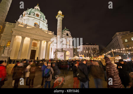 Popular Christkindlmarkt at Karlsplatz with crowd of tourists and people in festive Christmas mood. Karlskirche (St. Charles's Church) in background Stock Photo