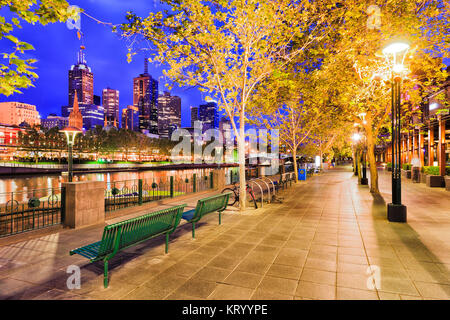Boardwalk for shoppers on southbank yarra river side in Melbourne city CBD at sunrise under leafy trees and illuminated street lamps. Stock Photo
