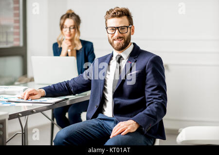 Portrait of a businessman dressed in suit working on documents with female assistant on the background at the white office interior Stock Photo