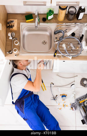 Male Plumber In Overall Fixing Sink Pipe Stock Photo