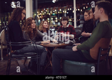 Group of positive teenagers spend time in cafe.