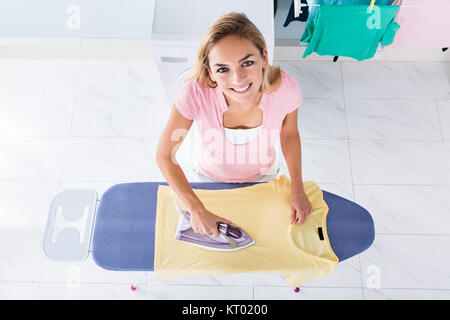 Woman Ironing T-shirt On Ironing Board At Home Stock Photo