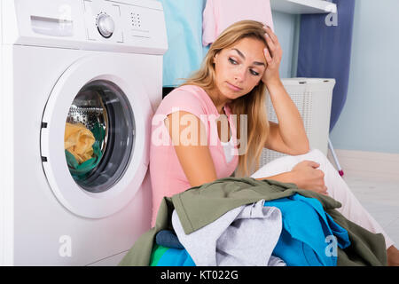 Unhappy Woman Looking At Clothes In Utility Room Stock Photo