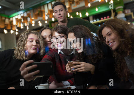 Group of positive teenagers make selfies and spending time in a cafe.