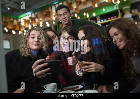 Group of positive teenagers make selfies and spending time in a cafe.