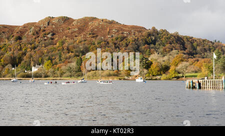 People row boats at Waterhead on Windermere lake, beside autumn woodland and under the hills of England's Lake District National Park. Stock Photo