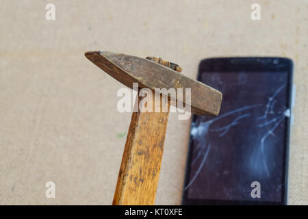 Hammer and smartphone. The screen of the smartphone, a broken ha Stock Photo