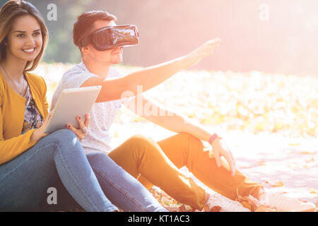 Couple sitting outside using various tech gadgets, tablet, vr, concept Stock Photo