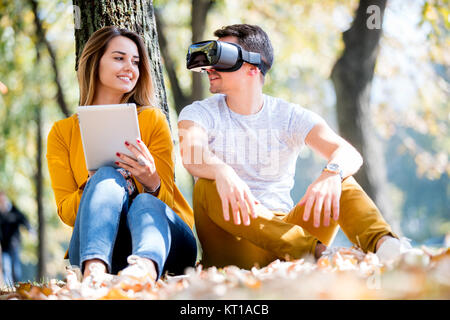Couple sitting outside using various tech gadgets, tablet, vr, concept Stock Photo