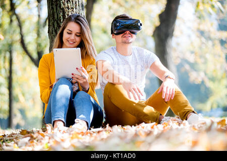 Couple sitting outside using various tech gadgets, tablet, vr, concept Stock Photo