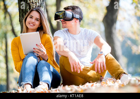 Couple sitting outside using various tech gadgets, tablet, vr, concept Stock Photo