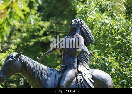 Native American Warrior Chie on horse looking up to heaven statue among green bokeh branches in Woodward Park Tulsa Oklahoma USA 8-27-2017 Stock Photo