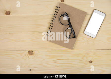 Mock up empty screen on mobile phone, eyeglasses on brown notepad, wooden table with copy space Stock Photo