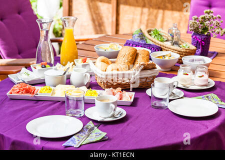 Fresh Breakfast or brunch with ham, eggs, bread, yogurt, fruits and coffee on violet table and white dishware Stock Photo