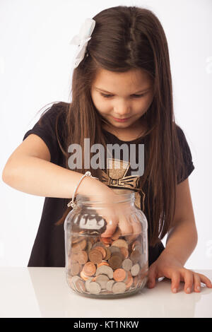 Seven year old girl with her hand in a clear glass jar full of coins. Stock Photo