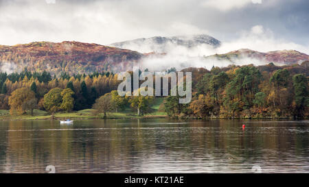 Mist rises from woodland in autumn colour at Ambleside on Windermere lake, under Wetherlam mountain in Langdale in England's Lake District National Pa Stock Photo