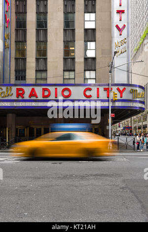 A yellow cab drives past the Radio City Music Hall building on 6th Avenue in Manhattan, New York, USA Stock Photo