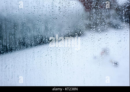 Water droplets running down a glass window on a snowy day Stock Photo