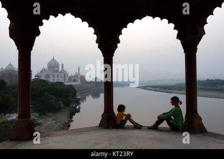 Mother and son sitting at pillars under an arch, looking at each other with an amazing view over Taj Mahal and Yamuna river, Agra,Uttar Pradesh, India. Stock Photo