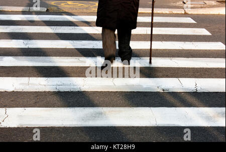 Legs and shadow of a senior person using walking cane while crossing the street Stock Photo